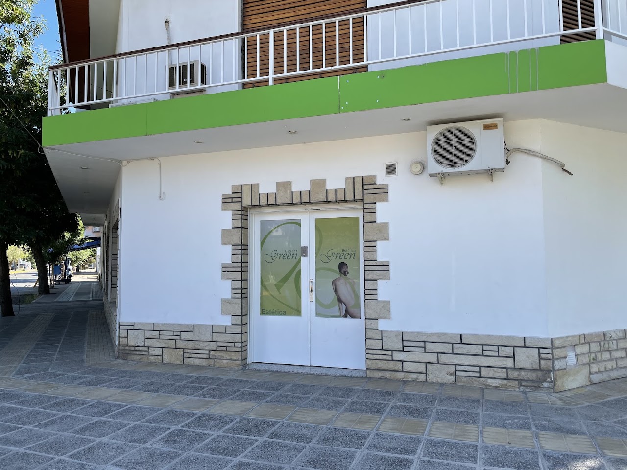 Exterior and welcoming reception entrance of an upscale, luxury boutique medical aesthetics and wellness spa clinic named 'Estética Green'. Modern glass storefront, warm ambient indoor lighting, lush natural botanical plants and ferns, minimalist white and light oak wood textures with deep emerald green architectural accents. Photorealistic architectural photography, serene evening daylight, high resolution, elegant, authentic local business facade.
